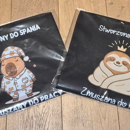 Two black pillowcases with Polish text and cartoon character designs featuring a baby and a sloth